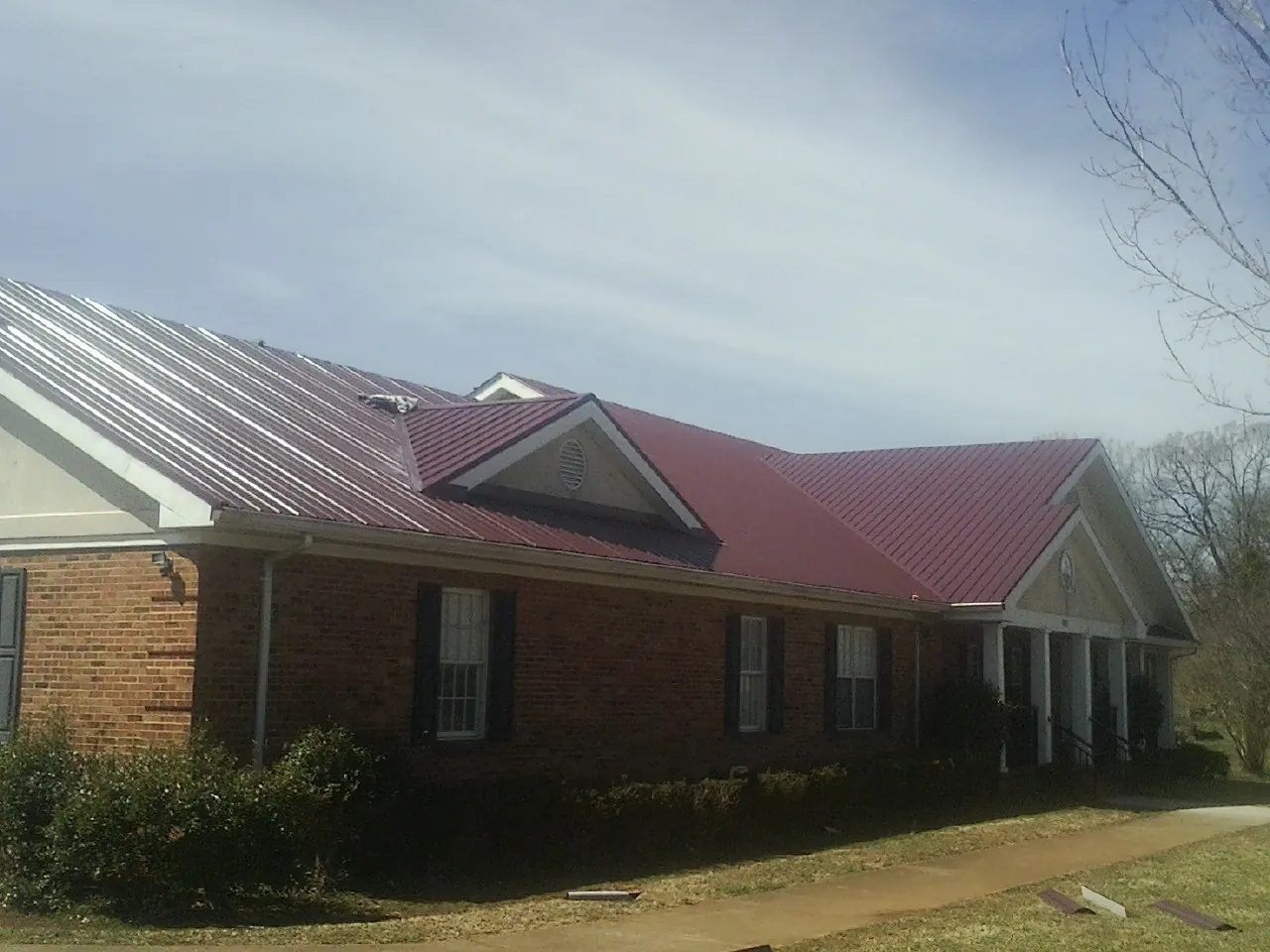 Red metal roof with gabled entries on a long brick building, from a Hail Damage Roof Repair job in East Waterford