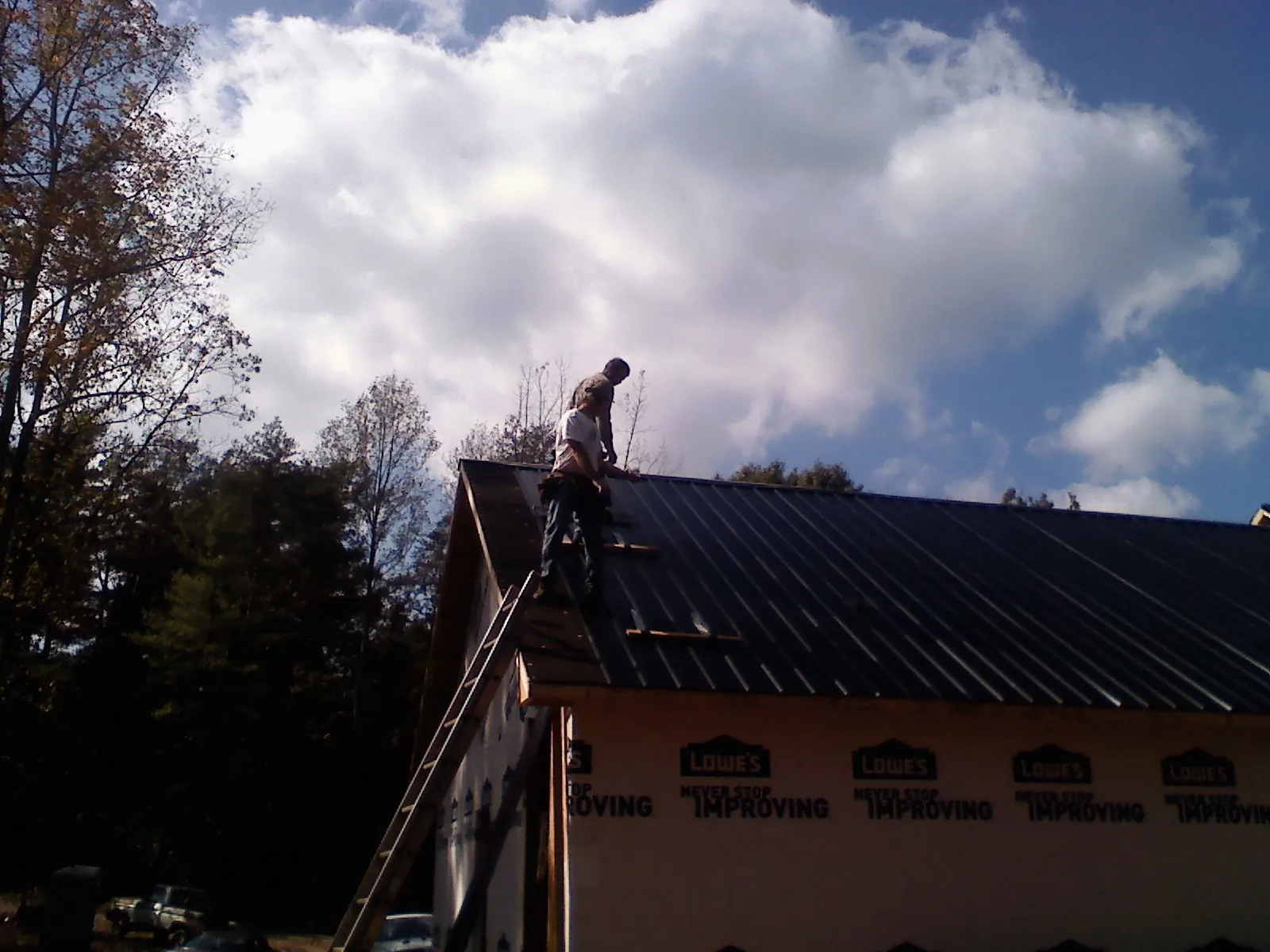 Roofer fastening dark metal panels high against a cloudy sky, from a Roof Inspection job in East Waterford