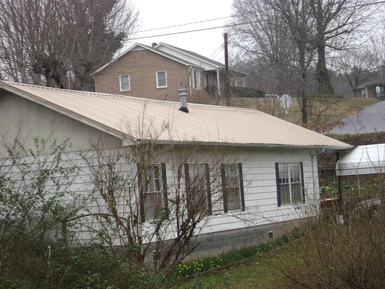 Tan metal roof on a white sided house set into a hillside — Commercial Roofing by Roofing Brothers in East Waterford
